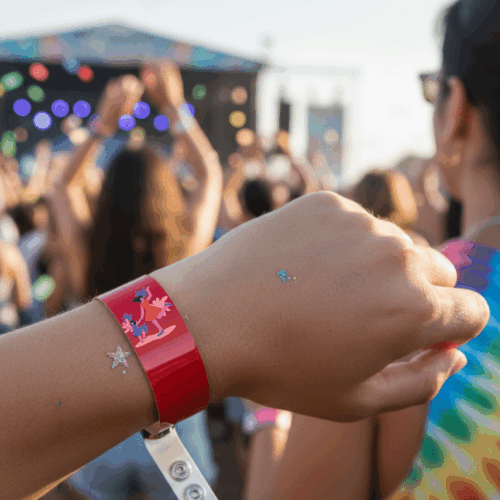 Attendee wearing a red custom vinyl wristband at an outdoor music festival with a stage and crowd in the background